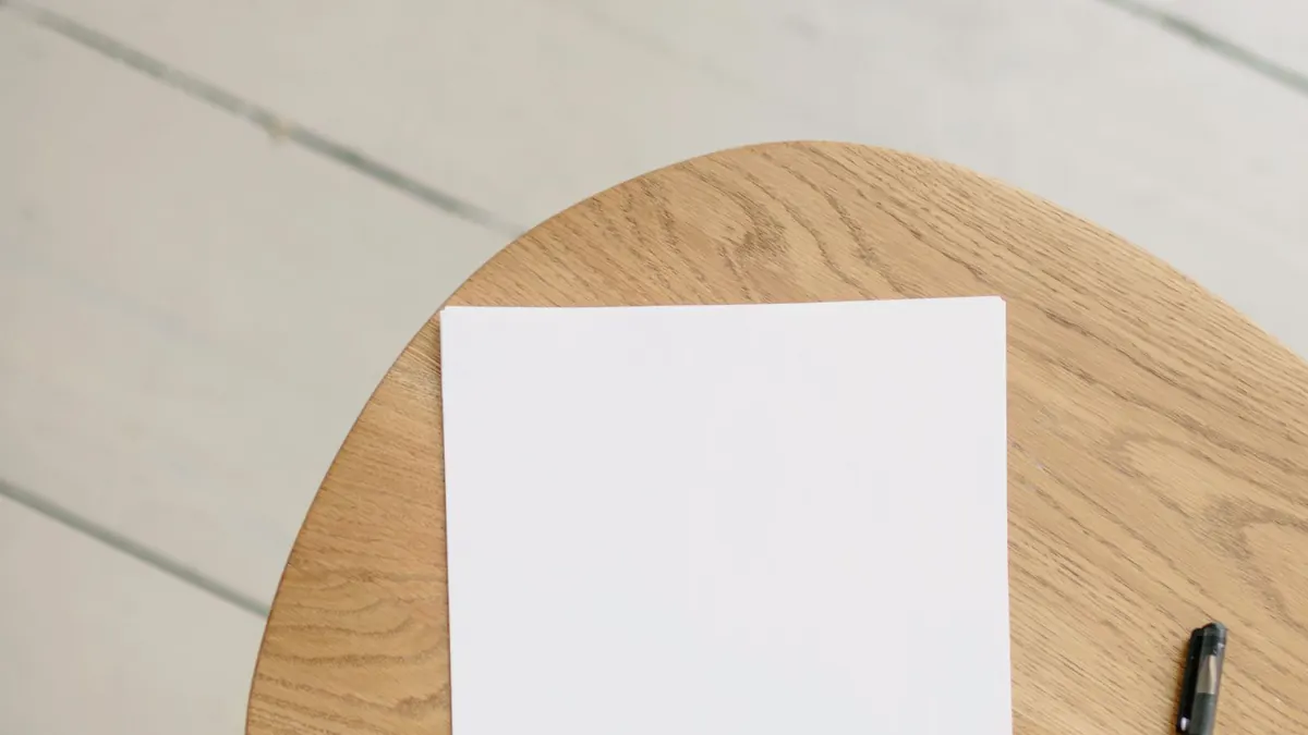 Blank white page and pen on a round wooden table